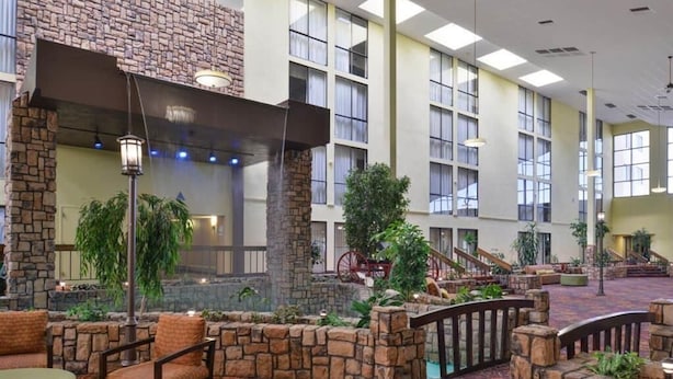 A spacious indoor lobby with stone walls, large windows, and a patterned carpet. - Ramada Plaza by Wyndham Sheridan Hotel & Convention Center (Sheridan)