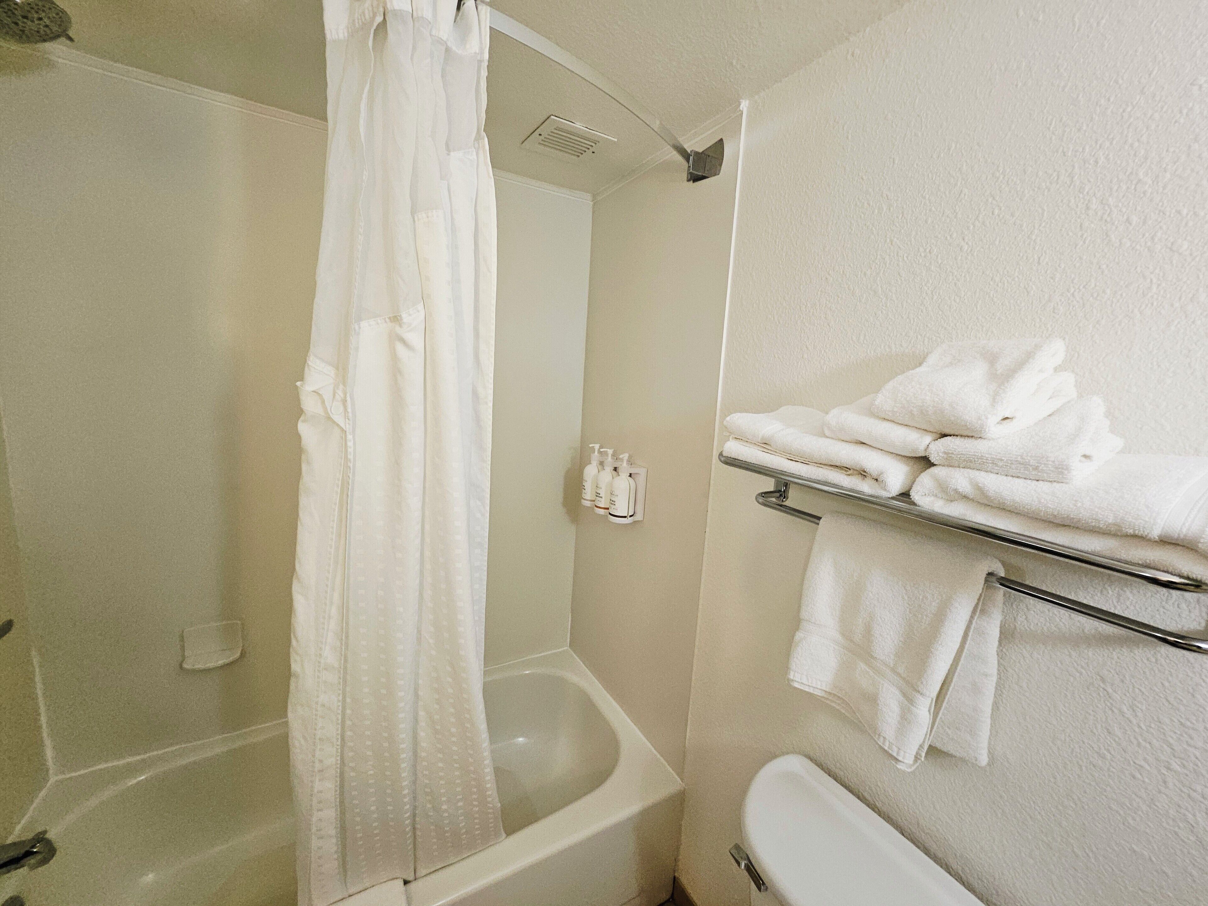 A bathroom with a bathtub, a shower curtain, a toilet, and a towel rack with folded towels.