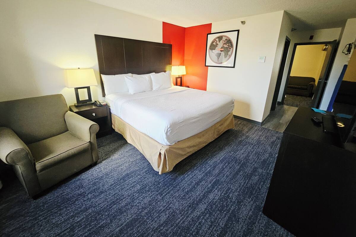 A hotel room with a large bed, a chair, a desk, and a lamp.