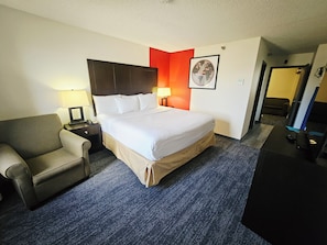 A hotel room with a large bed, a chair, a desk, and a lamp.