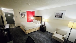 A hotel room with a bed, bedside tables, a chair, a desk, and a door. - Ramada Plaza by Wyndham Sheridan Hotel & Convention Center (Sheridan)