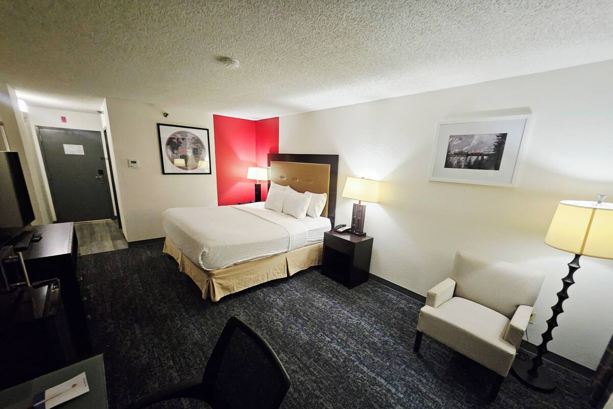 A hotel room with a bed, bedside tables, a chair, a desk, and a door.