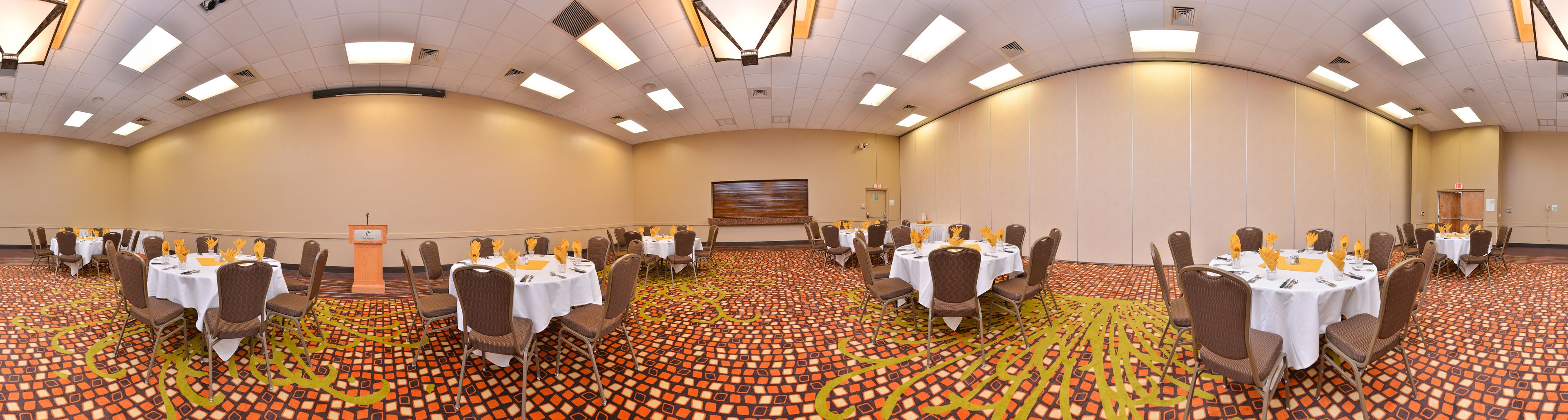 A conference room with multiple tables and chairs, a podium, and a patterned carpet.