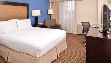 A hotel room with a large bed, a desk, a chair, a lamp, and a television.