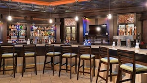 A bar area with multiple stools, a bar counter, and shelves stocked with bottles. - Ramada Plaza by Wyndham Sheridan Hotel & Convention Center (Sheridan)
