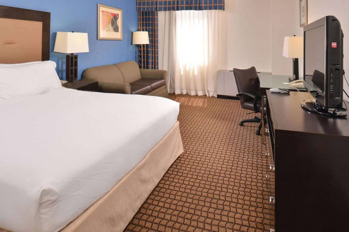 A hotel room with a large bed, a desk with a computer, a chair, and two lamps.