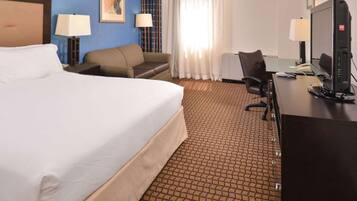 A hotel room with a large bed, a desk with a computer, a chair, and two lamps.
