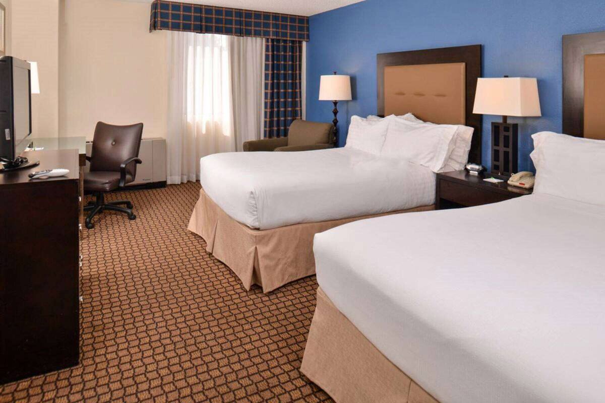 A hotel room with two beds, a desk, a chair, and a television.