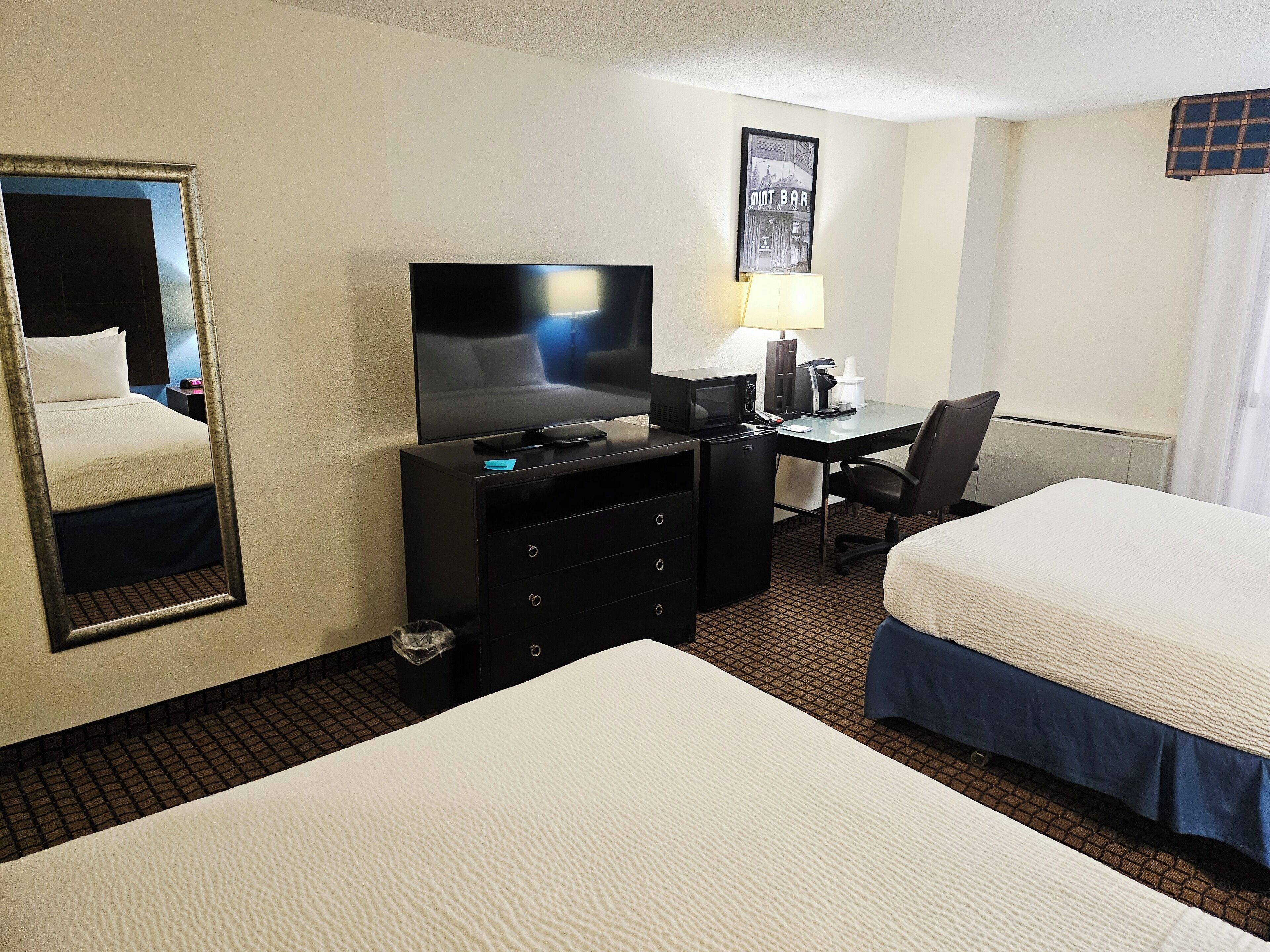 A hotel room with two beds, a desk with a computer, a television, a mirror, and a picture on the wall.