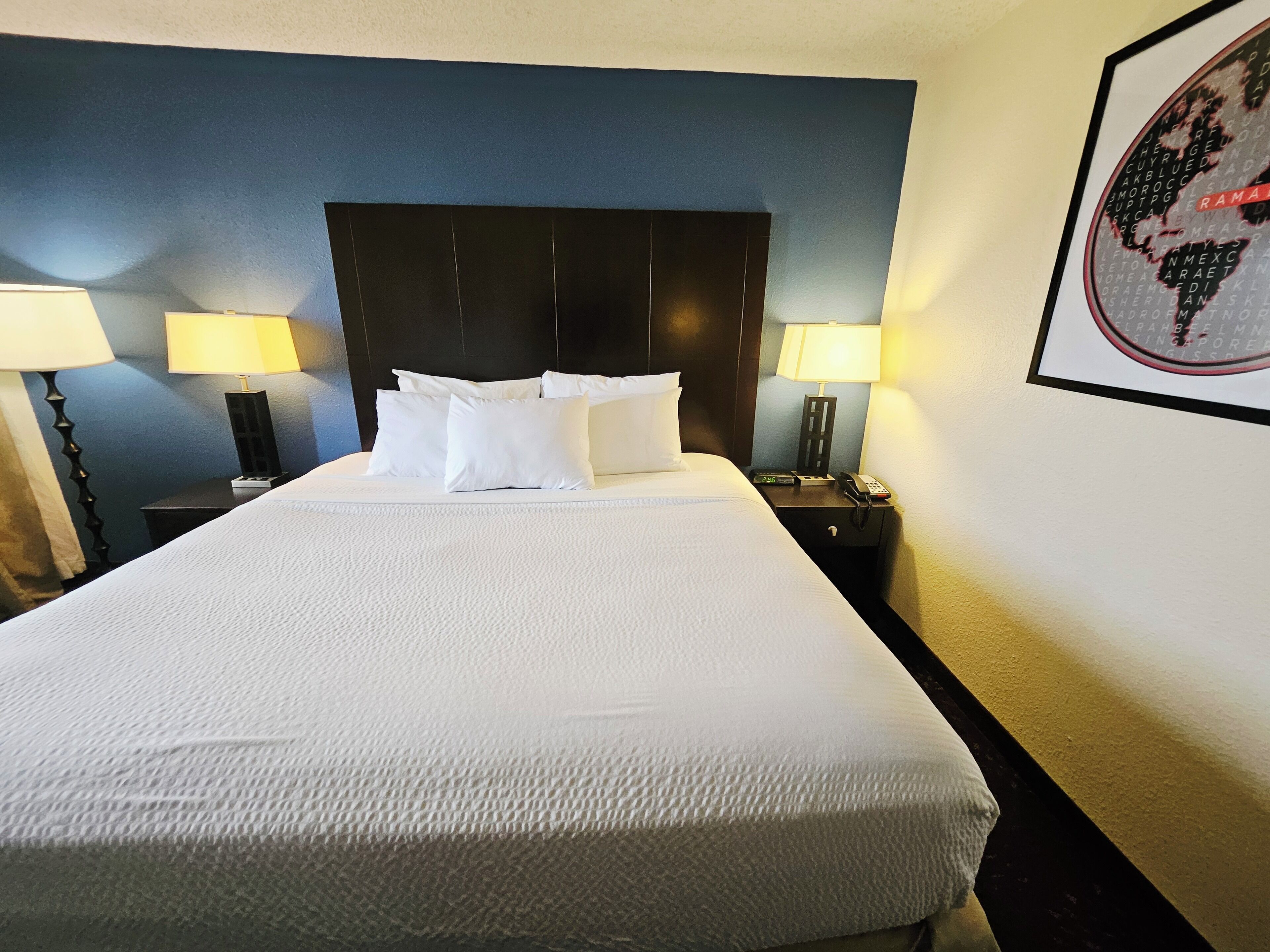 A neatly made bed with white linens, a dark headboard, and two bedside lamps.