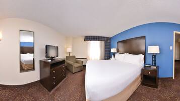 A hotel room with a large bed, a desk with a computer, a chair, a television, and a bathroom door.