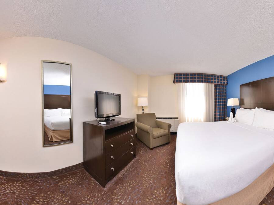 A hotel room with a large bed, a desk with a computer, a chair, a television, and a bathroom door.