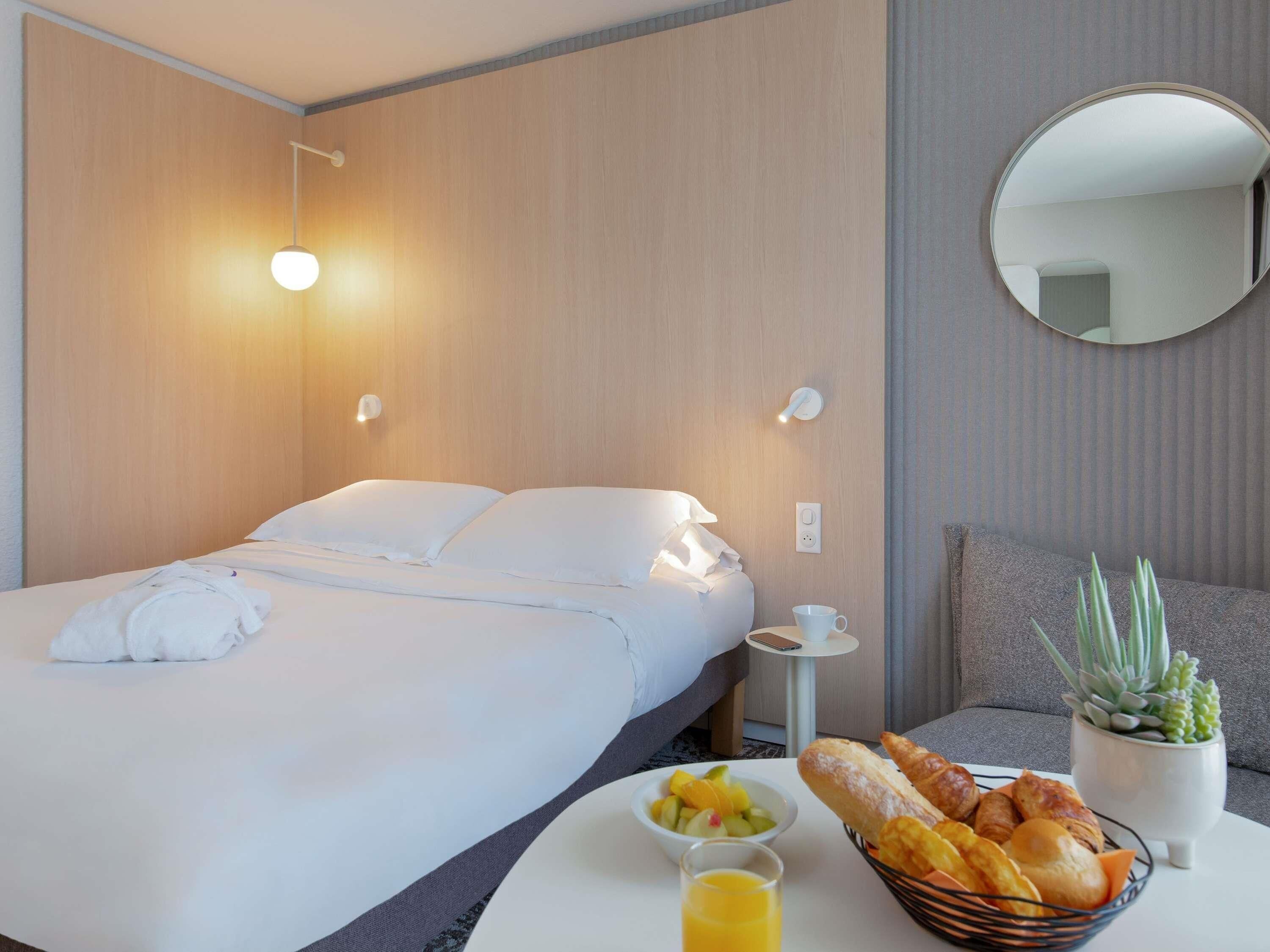 A hotel room with a bed, bedside table, and a small table with breakfast items.
