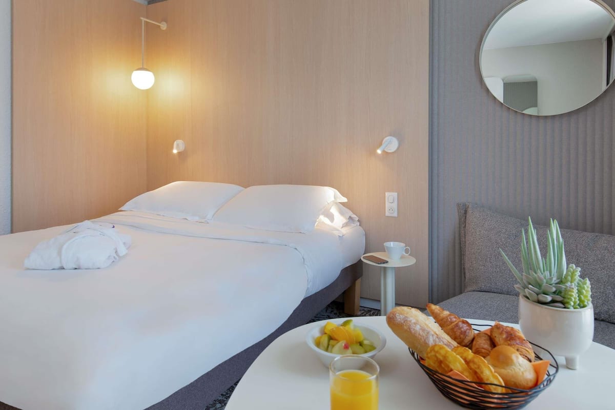 Une chambre d’hôtel avec un lit, une table de chevet et une petite table sur laquelle sont disposés des articles pour le petit-déjeuner.