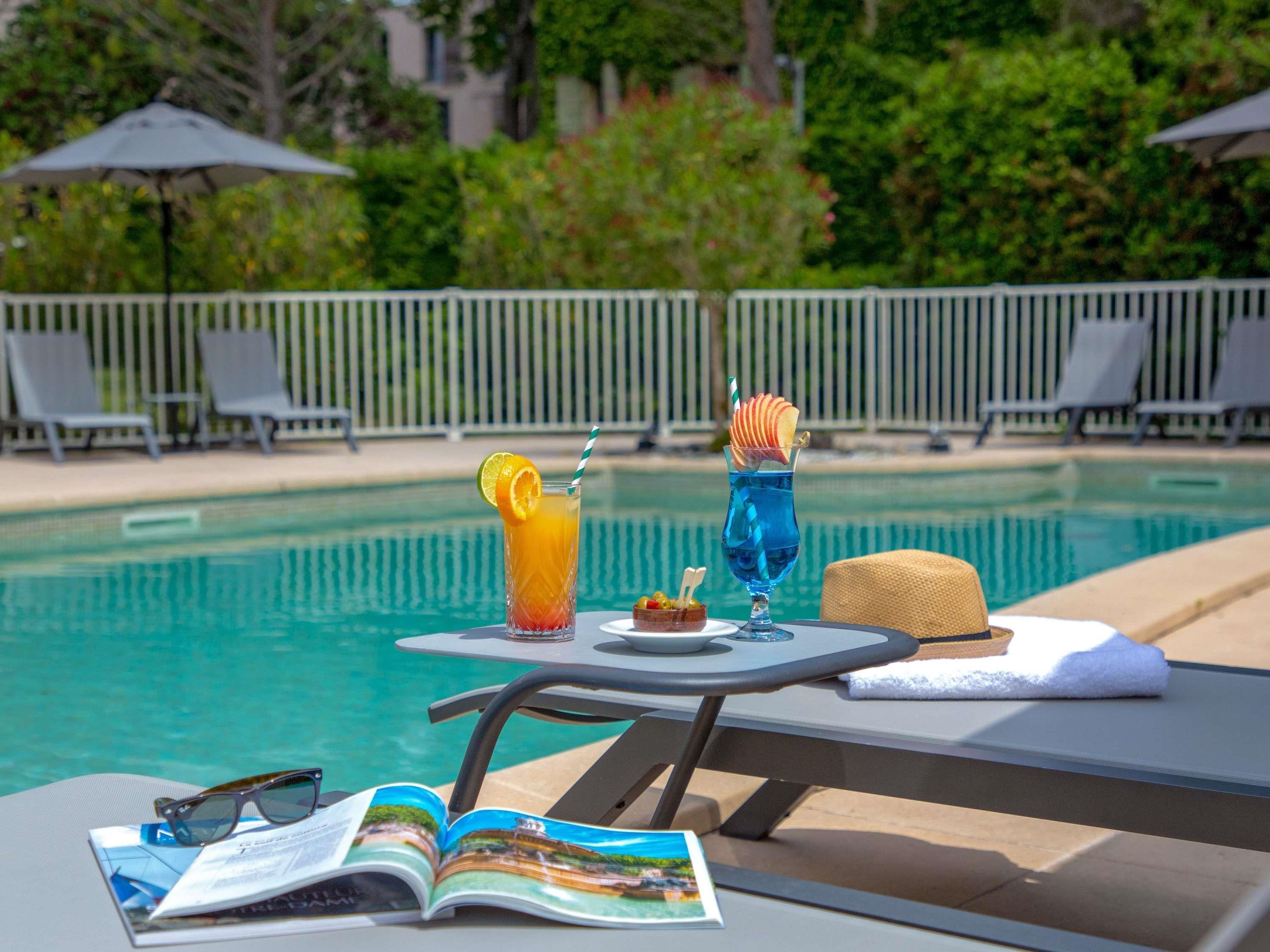 A poolside table with drinks, a magazine, and a pair of sunglasses.