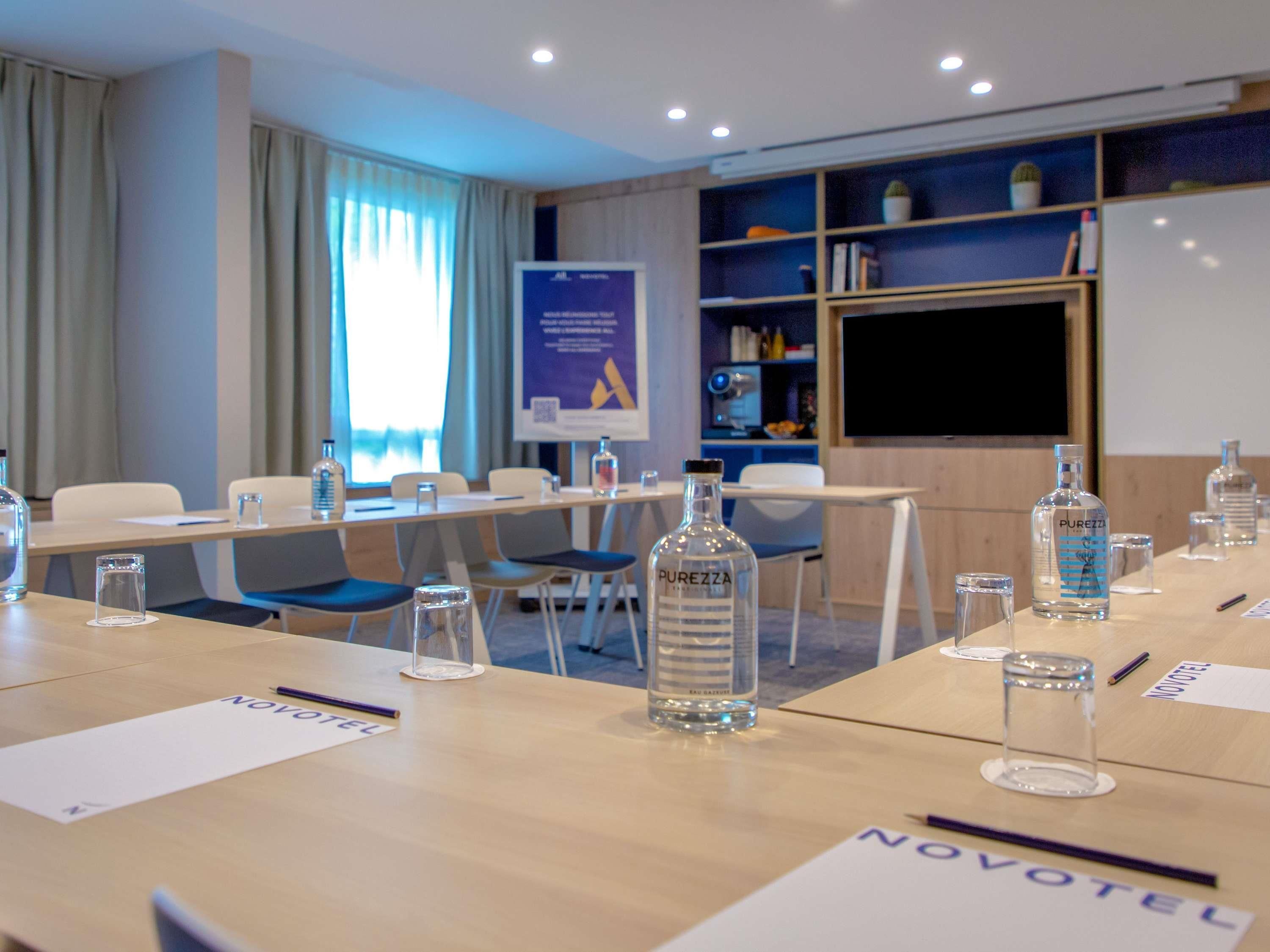 Un salón de conferencias de hotel con mesas, sillas, botellas de agua y una pantalla de proyector.