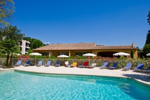 A swimming pool with lounge chairs and umbrellas, surrounded by a fence and greenery. - Hotel Novotel Aix en Provence Pont de l'Arc Fenouillères (Aix-en-Provence)