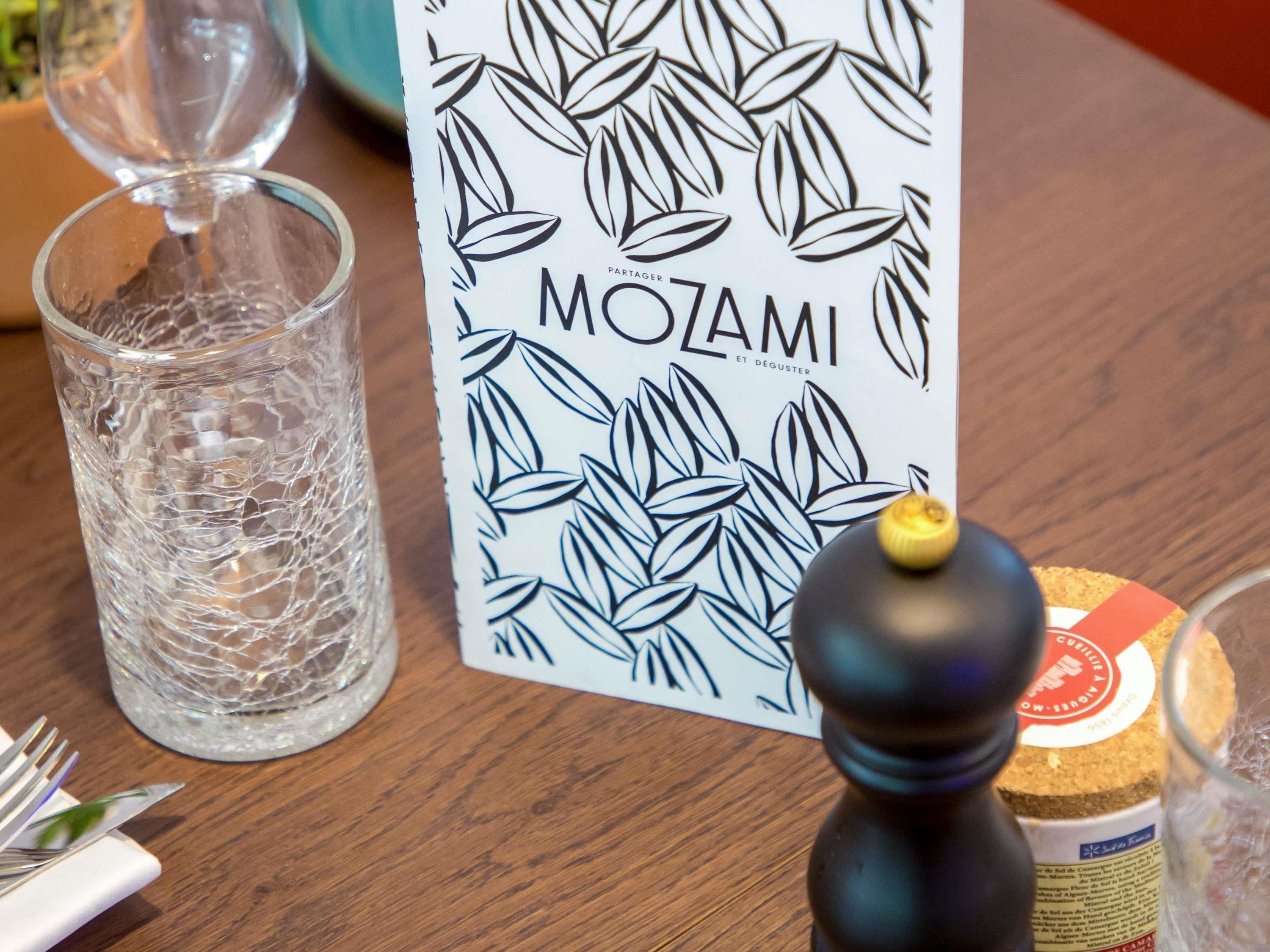 Una mesa con un vaso, una tarjeta con el texto 'MOZAMI', un molinillo de pimienta y una botella.