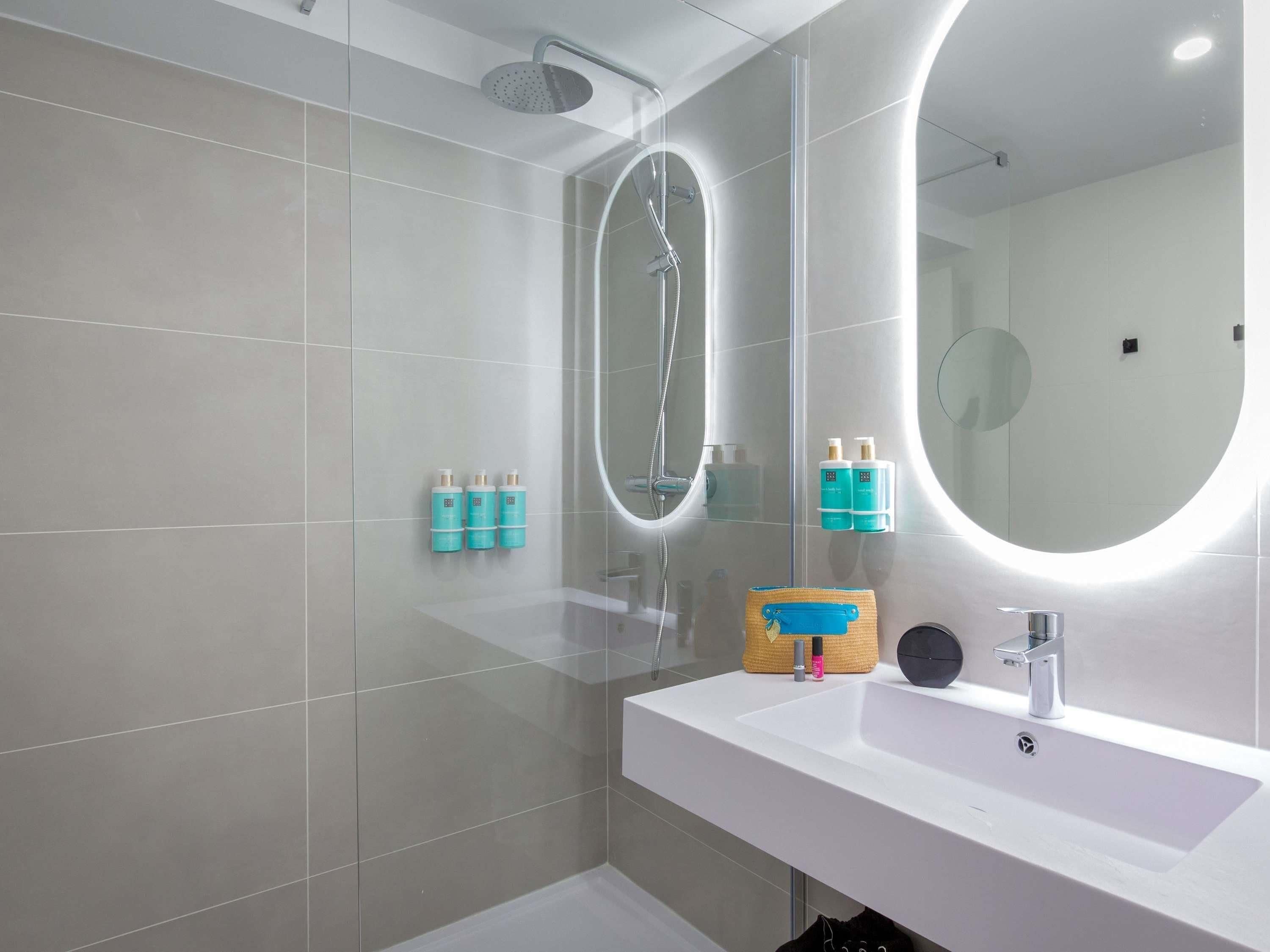 Une salle de bain moderne avec un grand miroir, une douche et un lavabo.