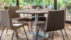 A modern outdoor dining area with a glass enclosure, providing a view of the surrounding greenery. - Hotel Novotel Aix en Provence Pont de l'Arc Fenouillères (Aix-en-Provence)