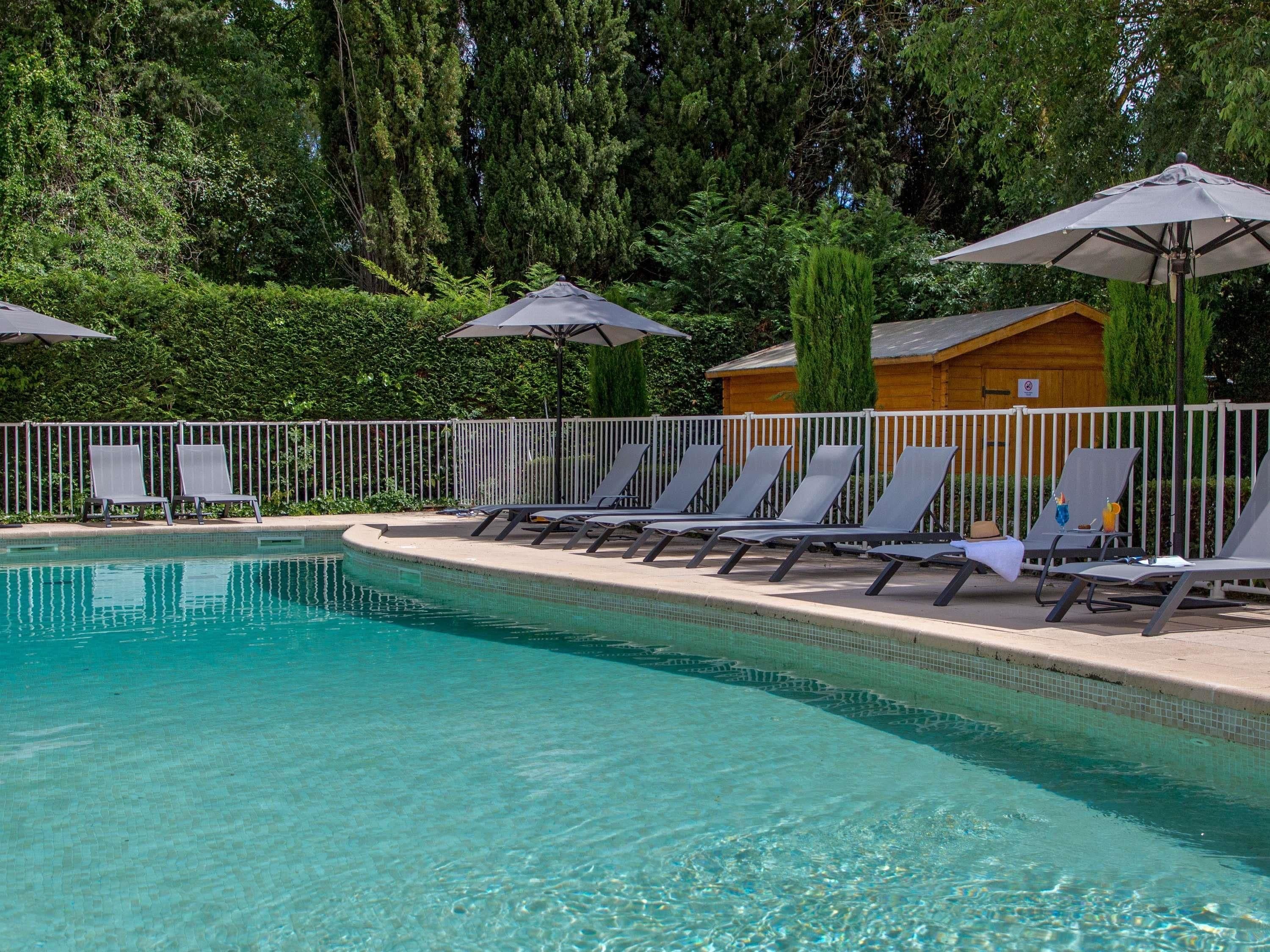 Area piscina con lettini e ombrelloni, circondata da una cabina in legno e vegetazione lussureggiante.