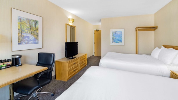 Habitación de hotel con dos camas, un escritorio con silla, televisor, cafetera y obras de arte en las paredes.