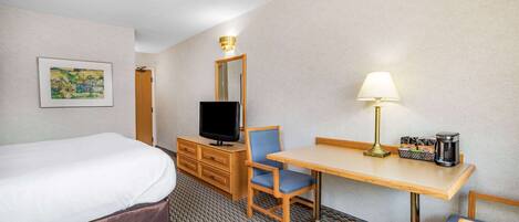 A hotel room with a bed, a desk with a lamp, a television, and a coffee maker.