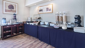 Montaje de un bufé de desayuno con diversos alimentos y bebidas, una máquina de café y un dispensador de agua.