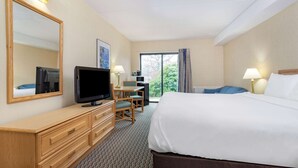 A hotel room with a large bed, a desk with a chair, a television, a dresser, and a window with curtains.