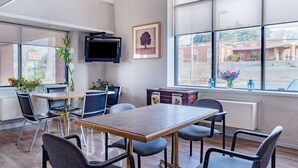 A conference room with a large table, chairs, a TV, and a window with a view of the outside.
