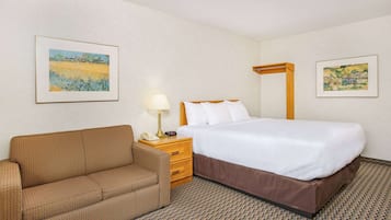 A hotel room with a bed, a sofa, a nightstand with a lamp, and two framed pictures on the walls.