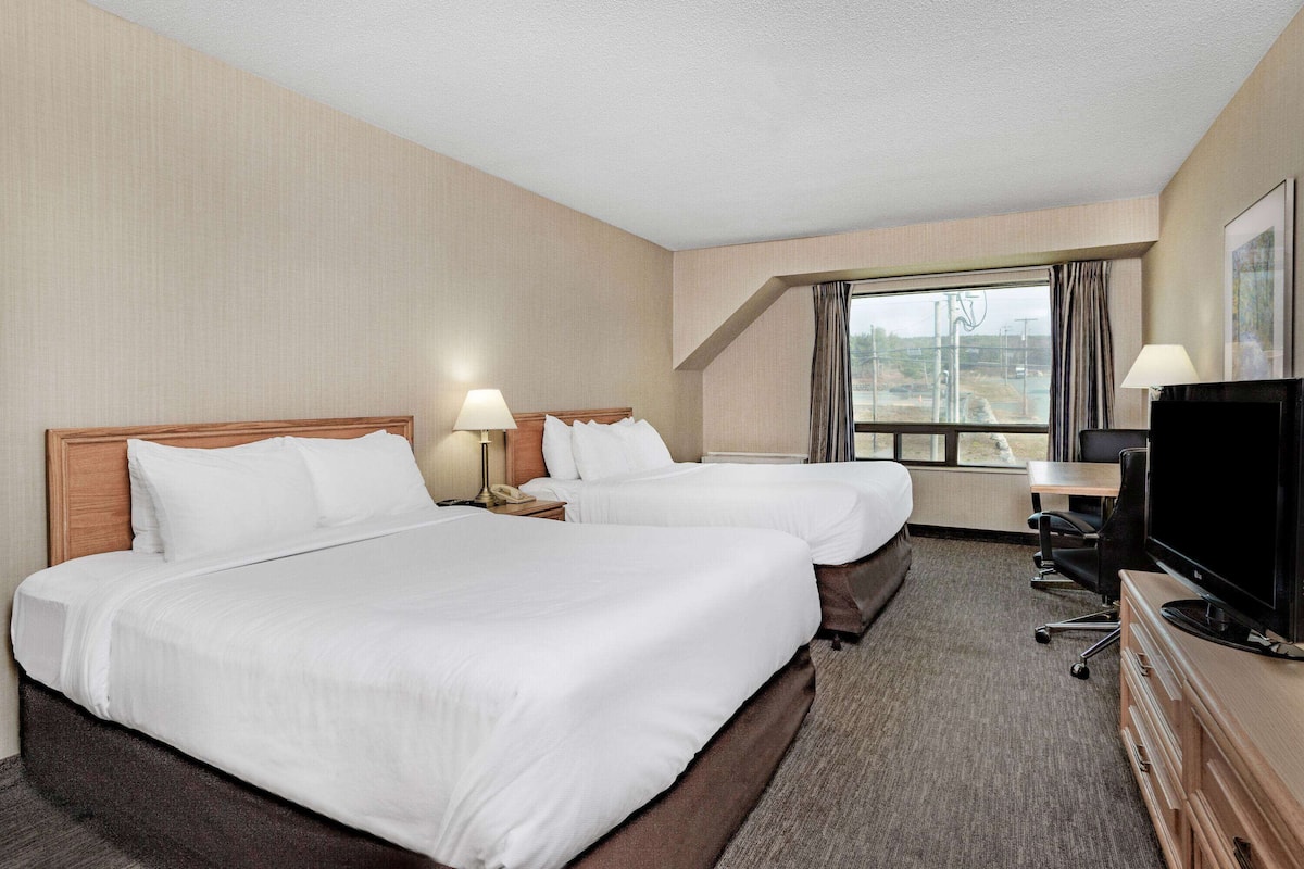 A hotel room with two beds, a desk, a TV, and a window with curtains.
