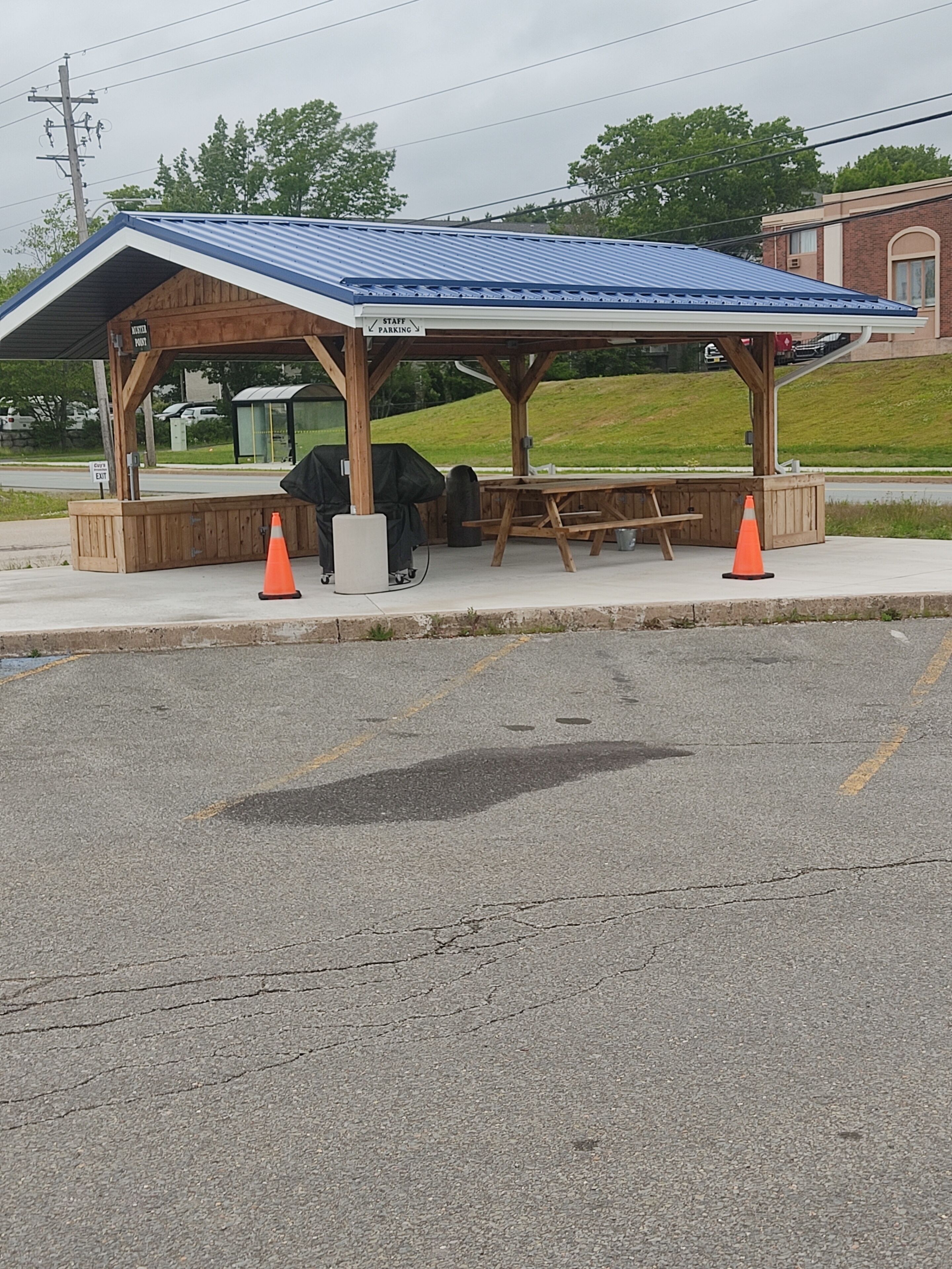 Un espace extérieur abrité avec des sièges, comprenant un banc et une table, une poubelle et un panneau indiquant les places de stationnement réservées au personnel.