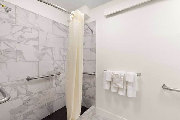 A bathroom with marble tiles, a shower curtain, handrails, and towels on a rack.