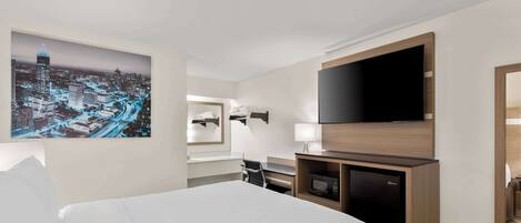 A hotel room with a large bed, a flat-screen TV, a microwave, and a cityscape painting on the wall.