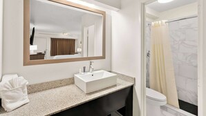 A bathroom with a white sink, a large mirror, a towel, and a shower with a curtain. - Clarion Pointe Kennesaw Town Center (Kennesaw)
