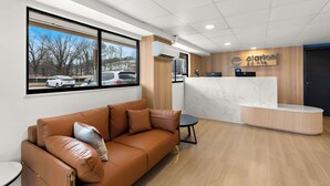 A modern reception area with a leather sofa, a reception desk, and a view of parked cars outside. - Clarion Pointe Kennesaw Town Center (Kennesaw)