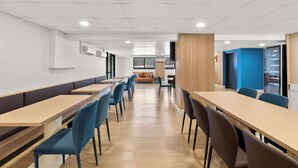 A modern dining area with long tables and chairs, a sofa, and a kitchen area in the background. - Clarion Pointe Kennesaw Town Center (Kennesaw)