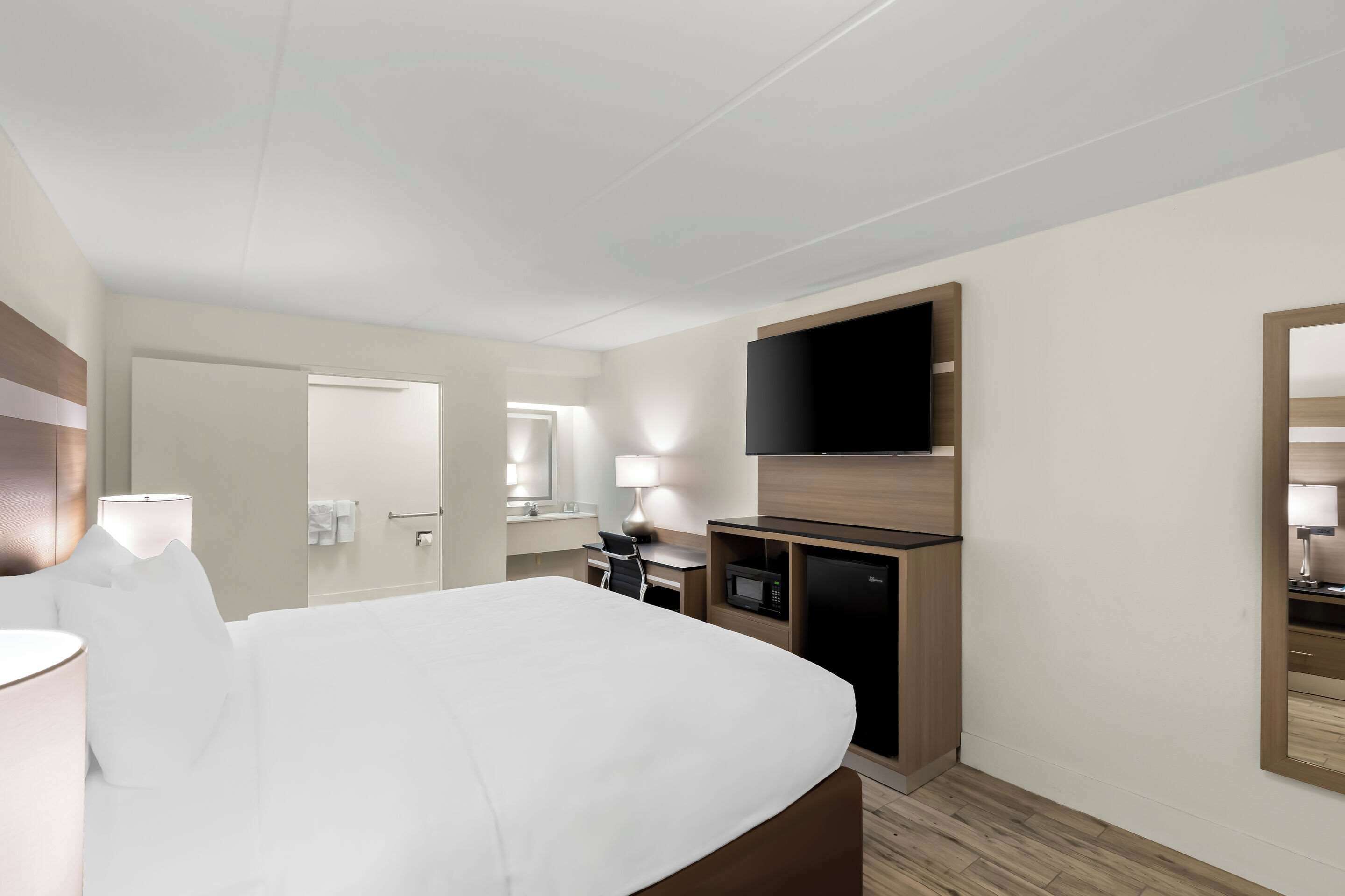 A hotel room with a bed, a desk, a flat-screen TV, a mirror, and a microwave.