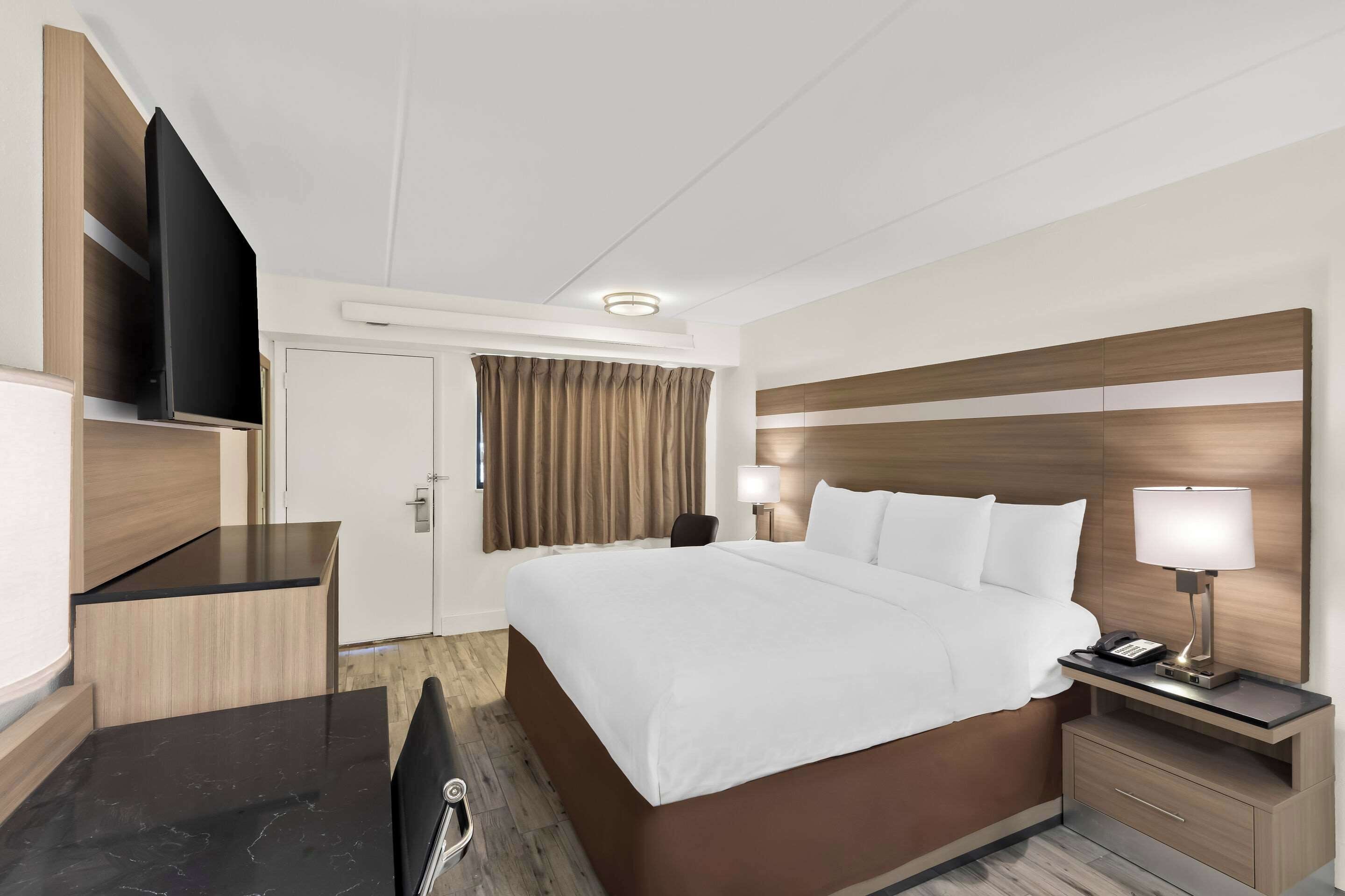 Une chambre d’hôtel comprenant un lit, des tables de chevet, un téléviseur fixé au mur et un bureau avec une chaise.