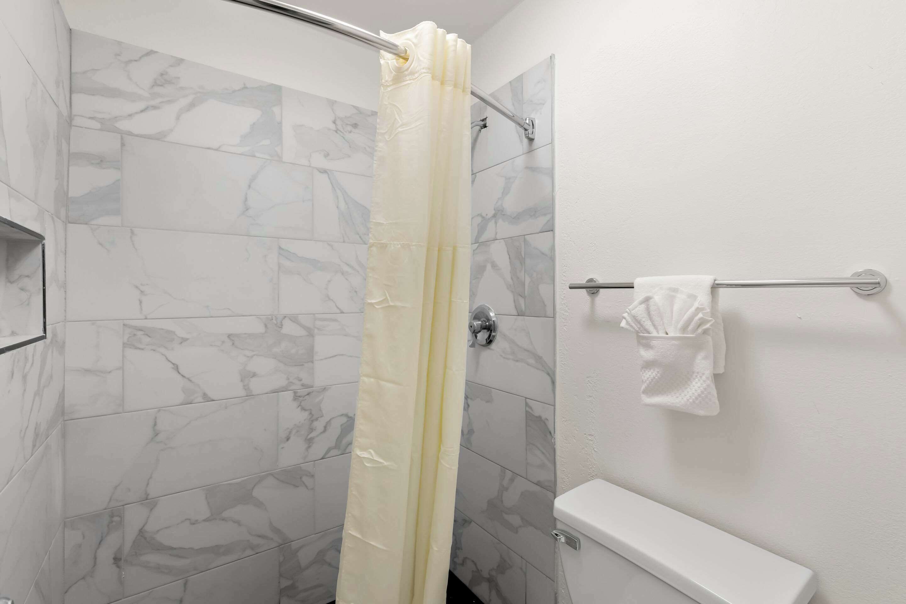 A bathroom with marble tiles, a shower curtain, a towel rack with a towel, and a toilet.