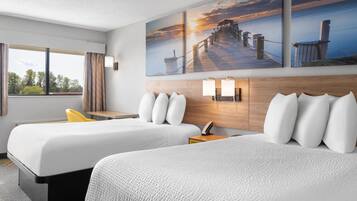 A hotel room with two beds, a wooden headboard, a nightstand with a lamp, and a window with curtains.