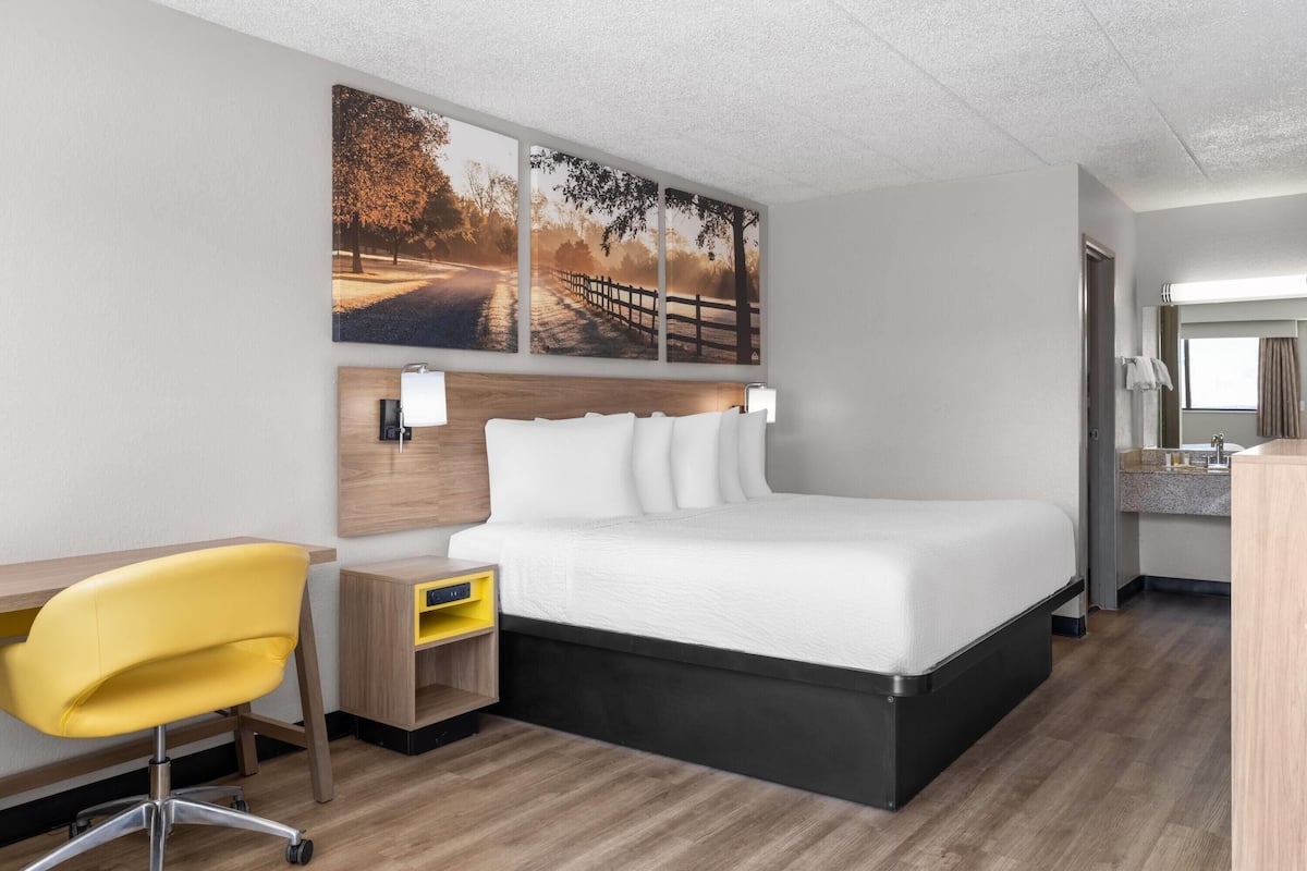 A hotel room with a bed, a desk, a chair, and a large window.