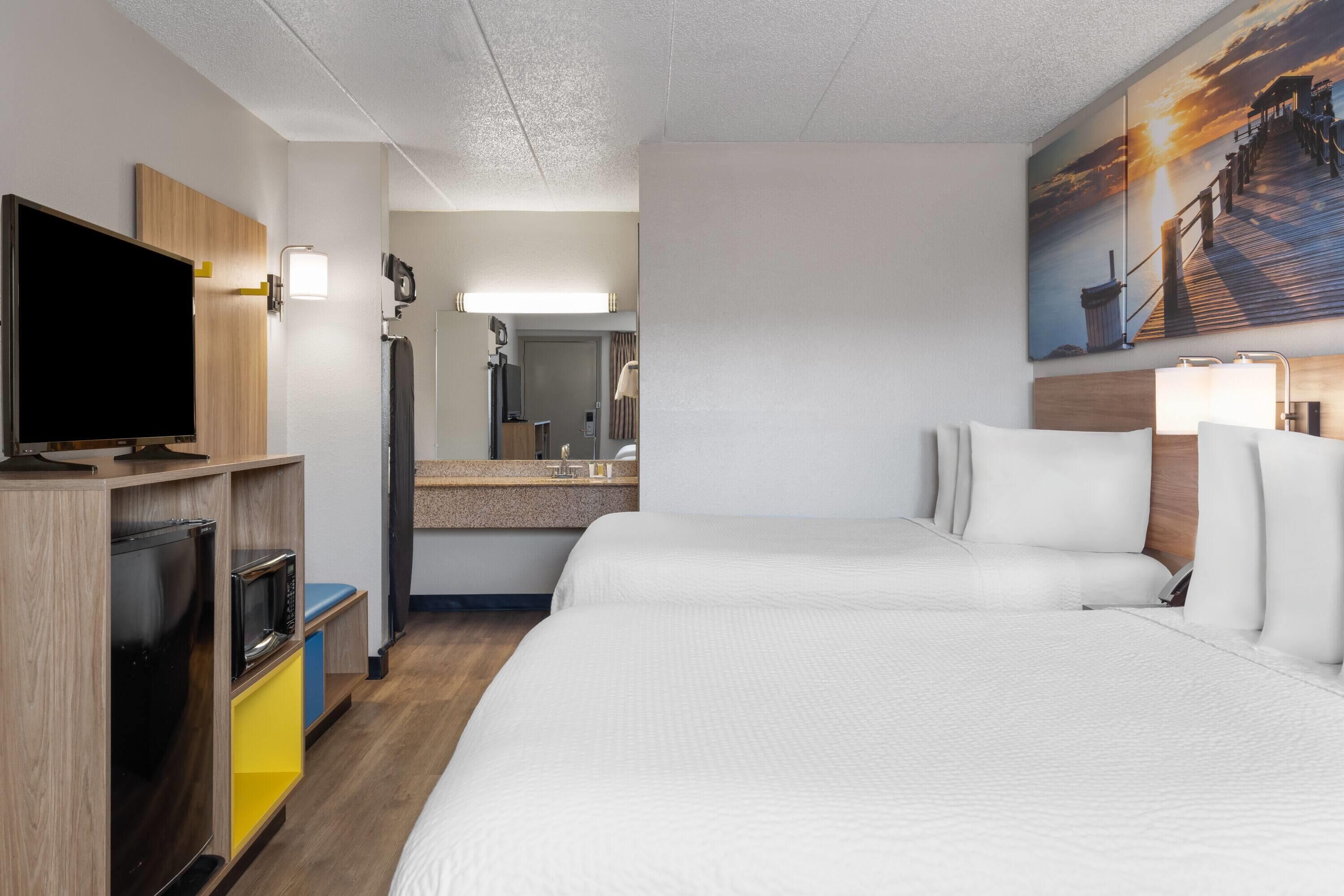 A hotel room with a large bed, a television, a desk with a computer, and a bathroom with a mirror and sink.