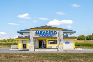 A Days Inn by Wyndham building with a modern design, featuring a prominent yellow and blue color scheme, a flat roof, and a visible Shell gas station sign. - Days Inn by Wyndham Cloverdale Greencastle (Cloverdale)