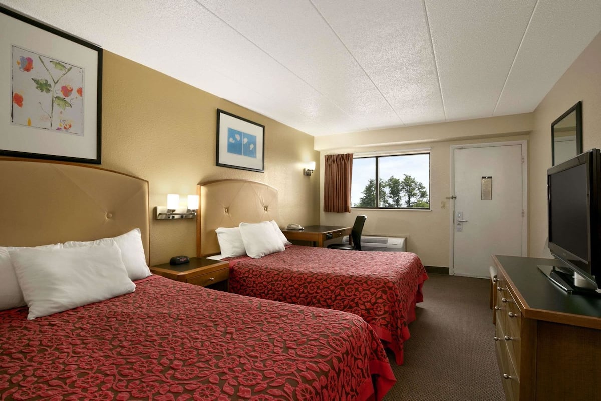 A hotel room with two beds, a desk, a television, and a window with a view.