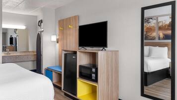 A hotel room with a bed, a flat-screen TV, a microwave, and a refrigerator.