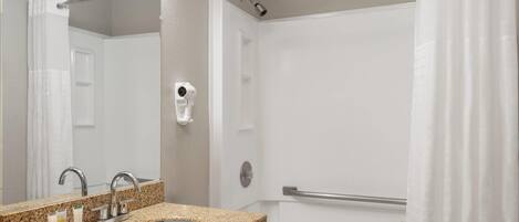 A bathroom with a granite sink, a mirror, a handheld showerhead, and a bathtub.