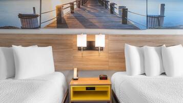 A hotel room with a wooden headboard, two white beds, a yellow nightstand with a lamp, and a painting of a pier at sunset.