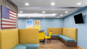 A modern interior with yellow and teal seating, a brick wall, and a mounted TV. - Days Inn by Wyndham Cloverdale Greencastle (Cloverdale)